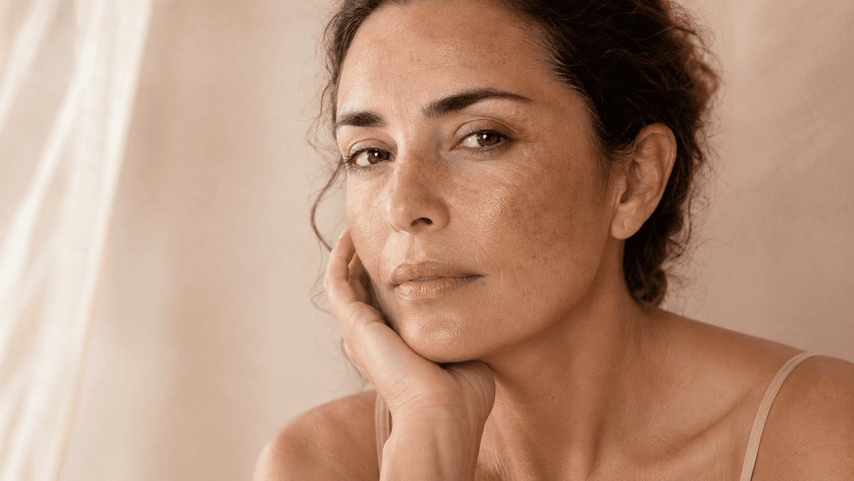 Close-up portrait of a woman with natural facial pigmentation, photographed in soft, warm light.