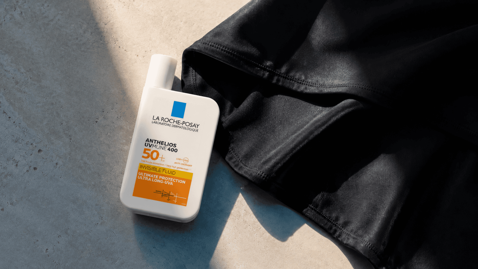 La Roche-Posay Anthelios SPF 50+ sunscreen placed beside black sun-protective fabric in warm natural light.