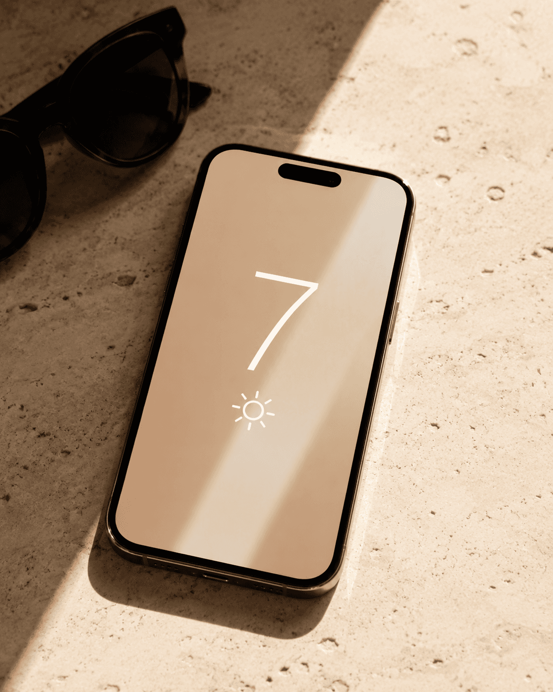 Smartphone displaying a UV Index of seven beside sunglasses in warm sunlight