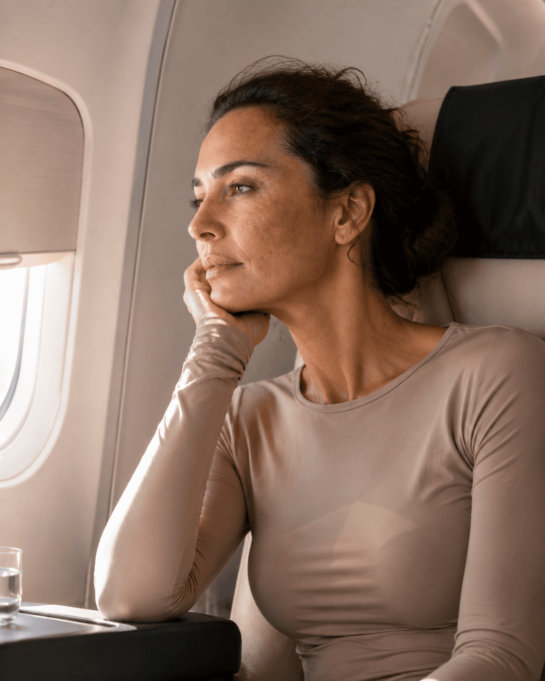 Woman wearing a long-sleeved protective top beside a partially shaded aeroplane window